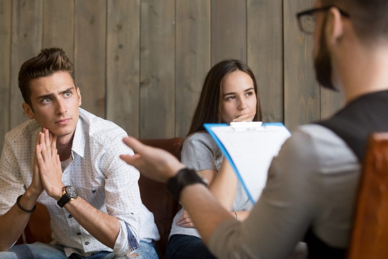 A man and woman sitting on the couch talking to another person.