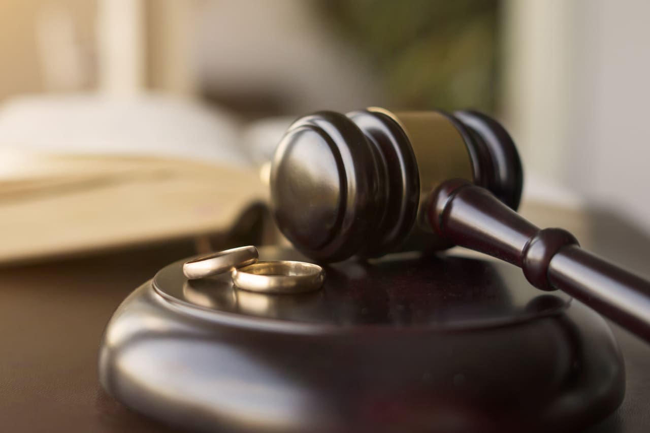 A judge 's gavel and two wedding rings on top of a wooden table.